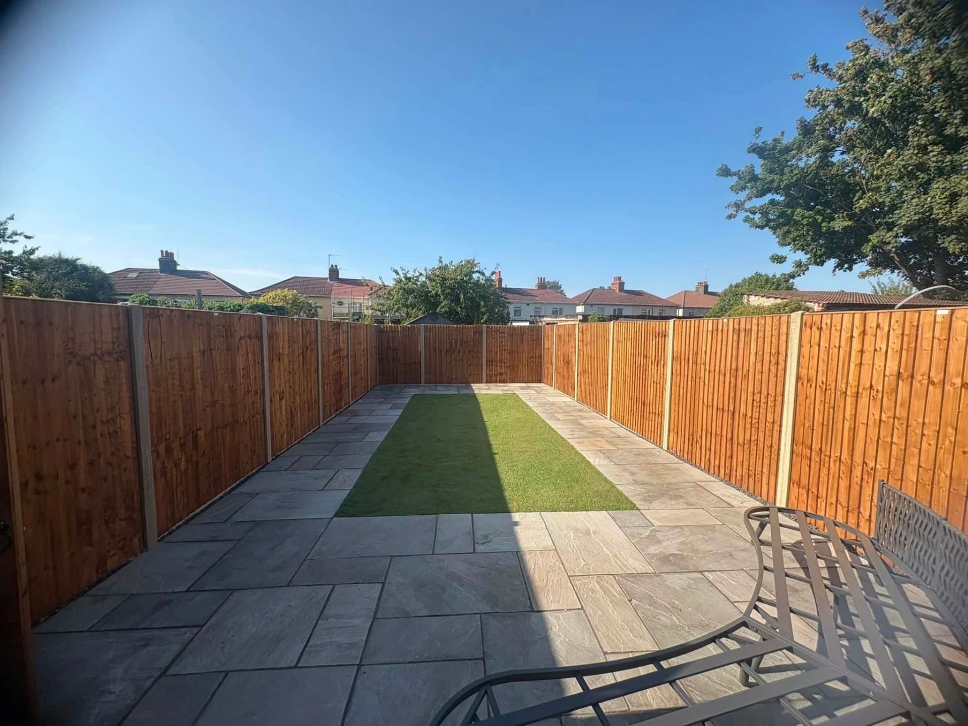 Grey paving patio with central artificial lawn strip and new fencing
