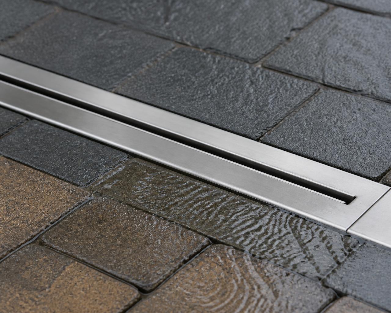 Neat stainless steel slot channel drain set into new block paving carrying water away